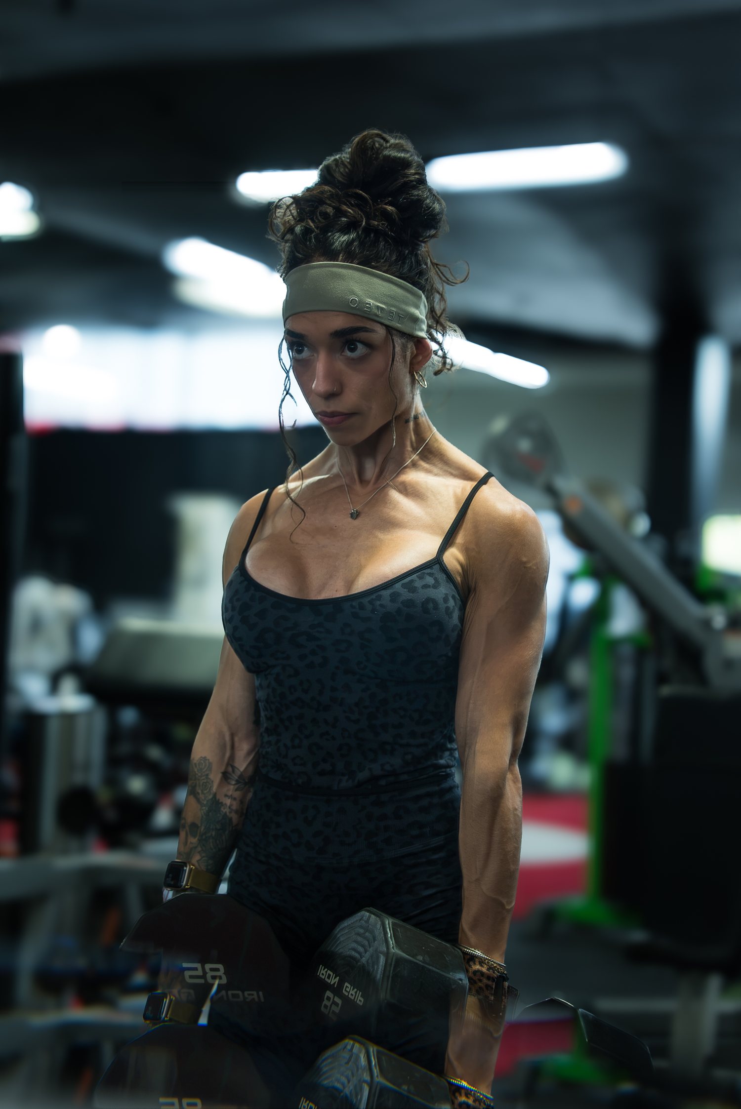 Roxy Cisneros holding a pair of dumbbells between sets, looking off to the side