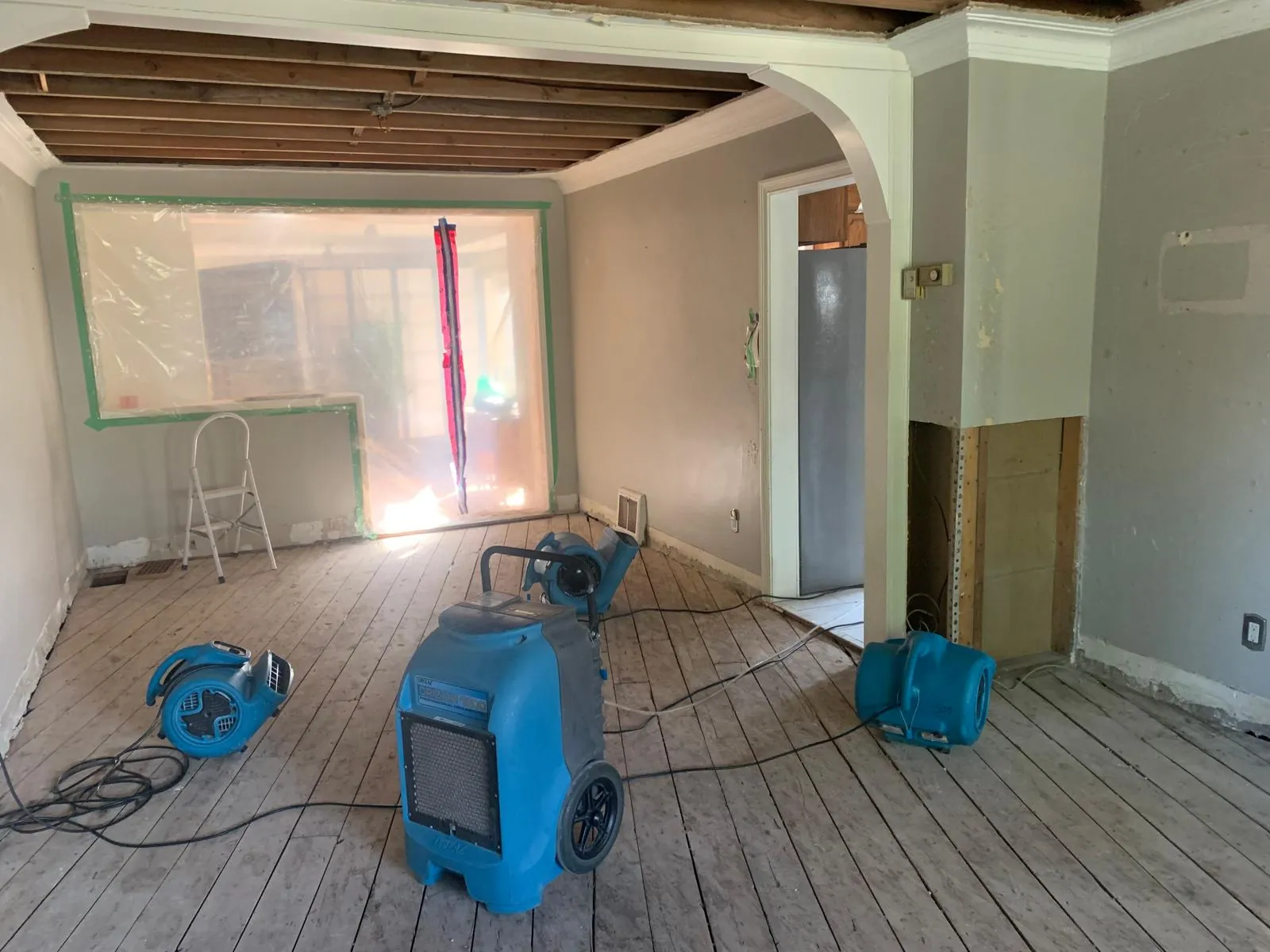Dehumidifier and air movers drying a stripped wood plank floor under an opened ceiling, South Florida