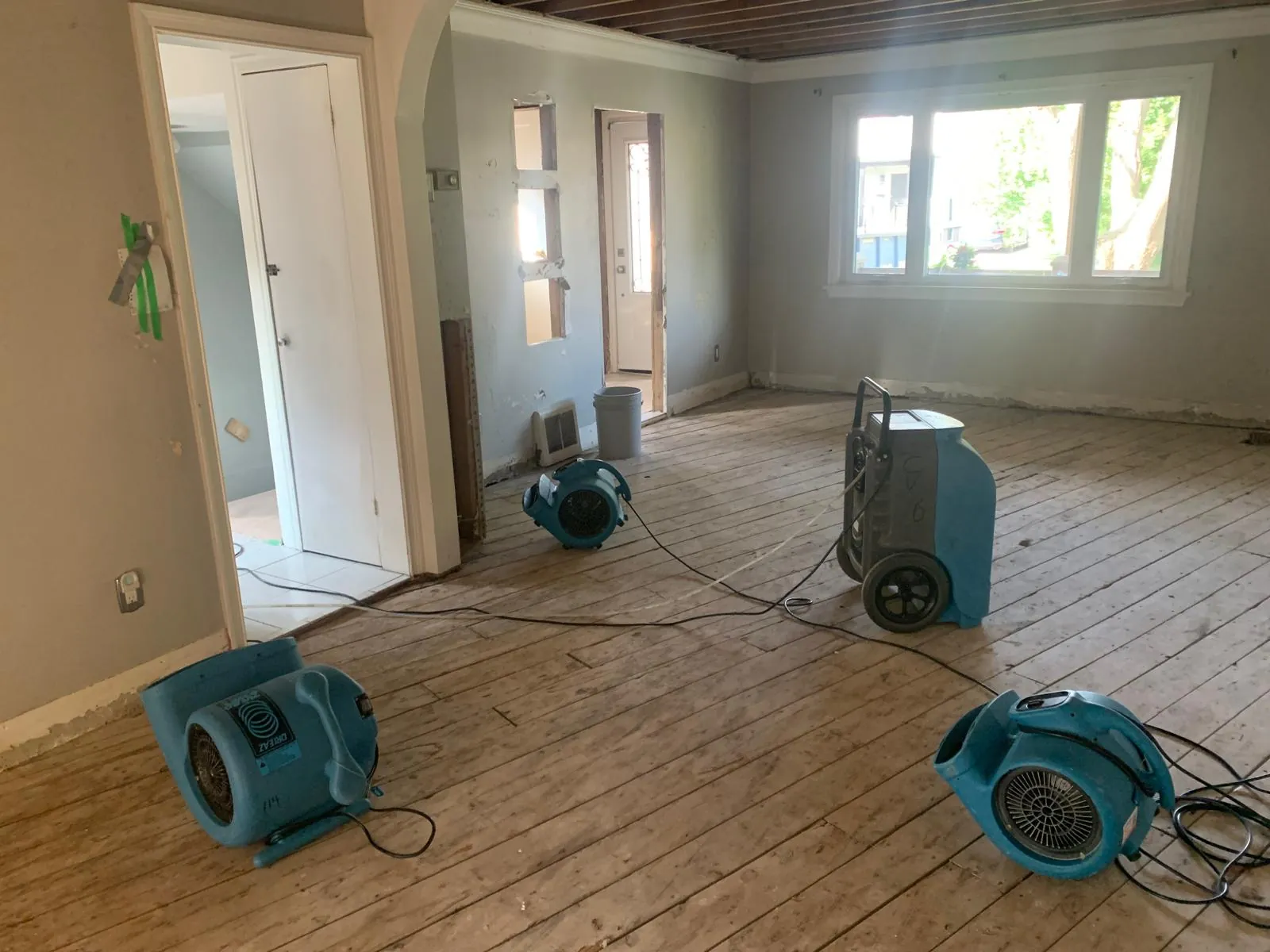 Dehumidifier and air movers drying an open living area with bare wood floors in South Florida