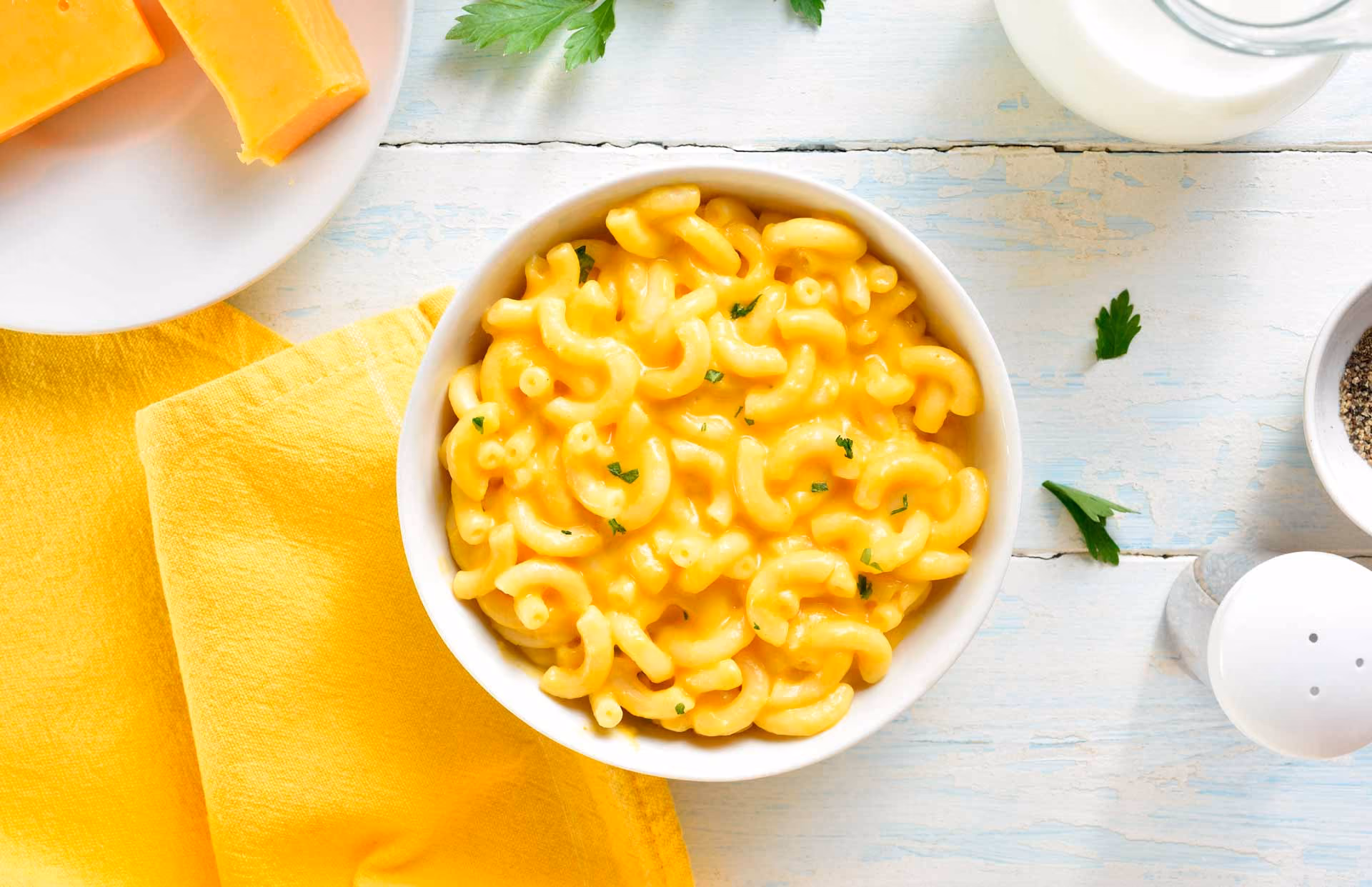 Bowl of creamy macaroni and cheese garnished with parsley on a light wooden surface.