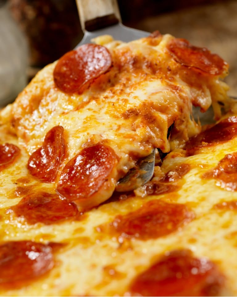 Slice of pepperoni pizza being lifted with melted cheese stretching.