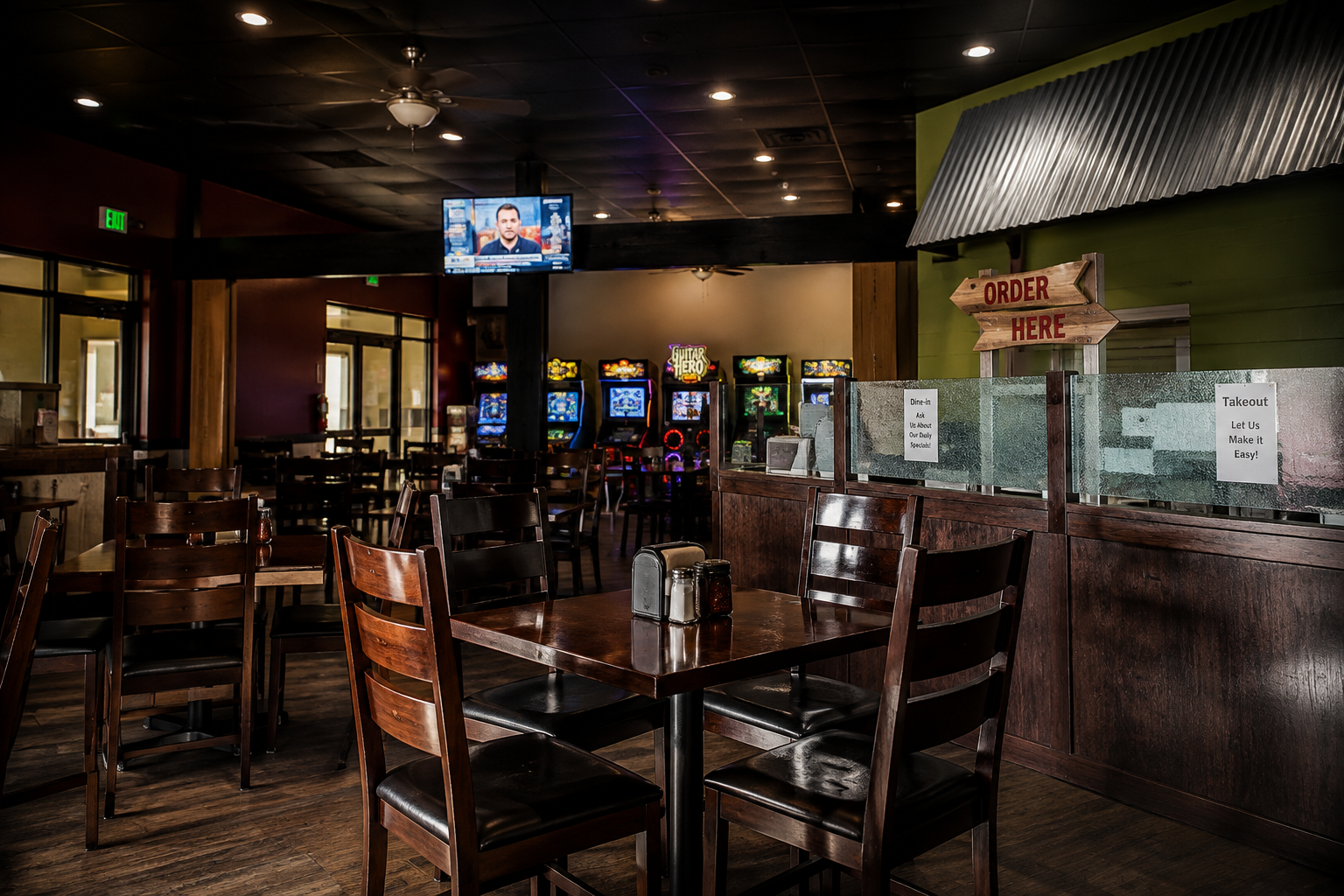 Empty restaurant with wooden tables, chairs, arcade games in back, and an 'Order Here' sign.