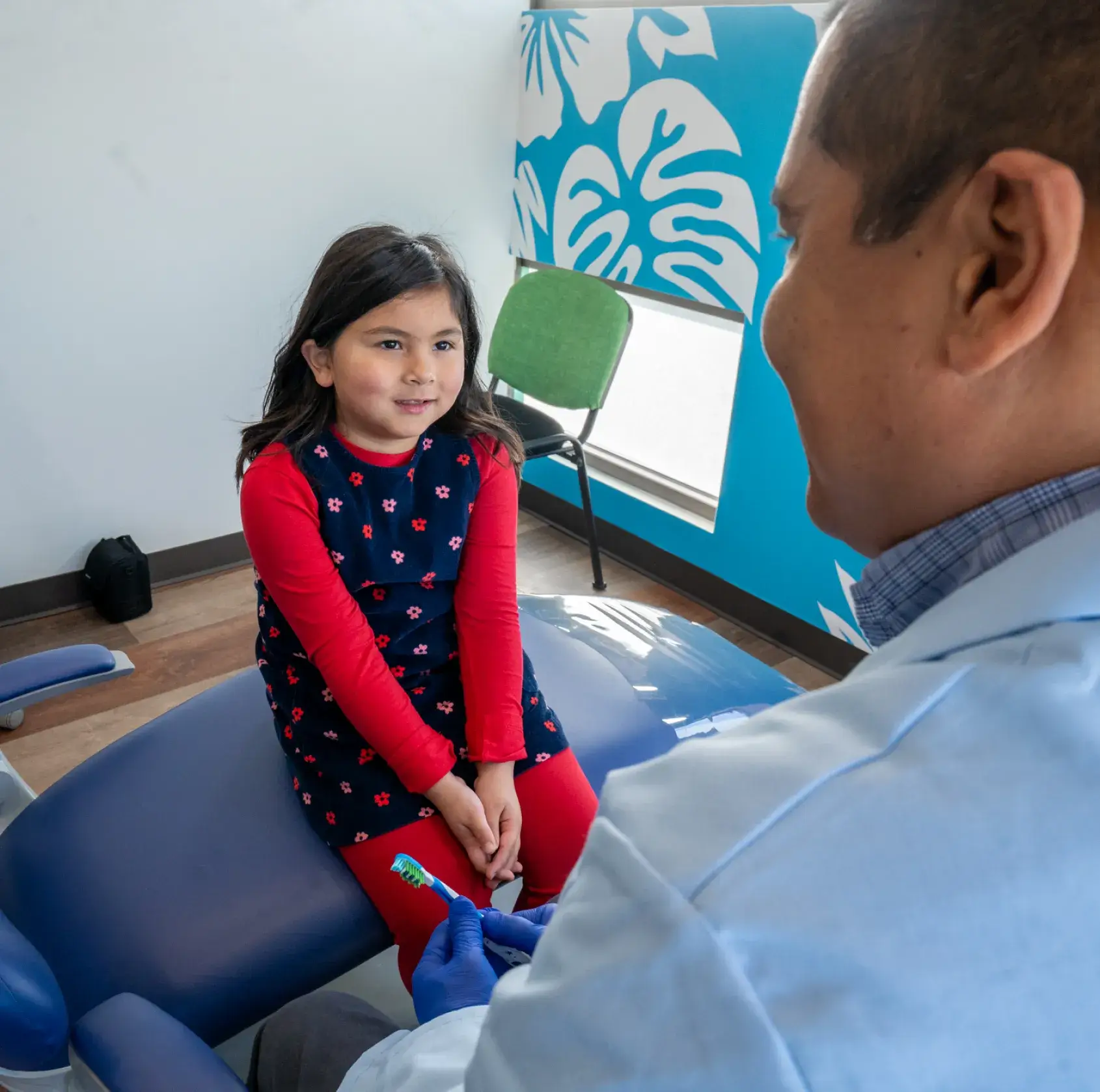 A little girl sitting on a blue chair in a dentist's office.