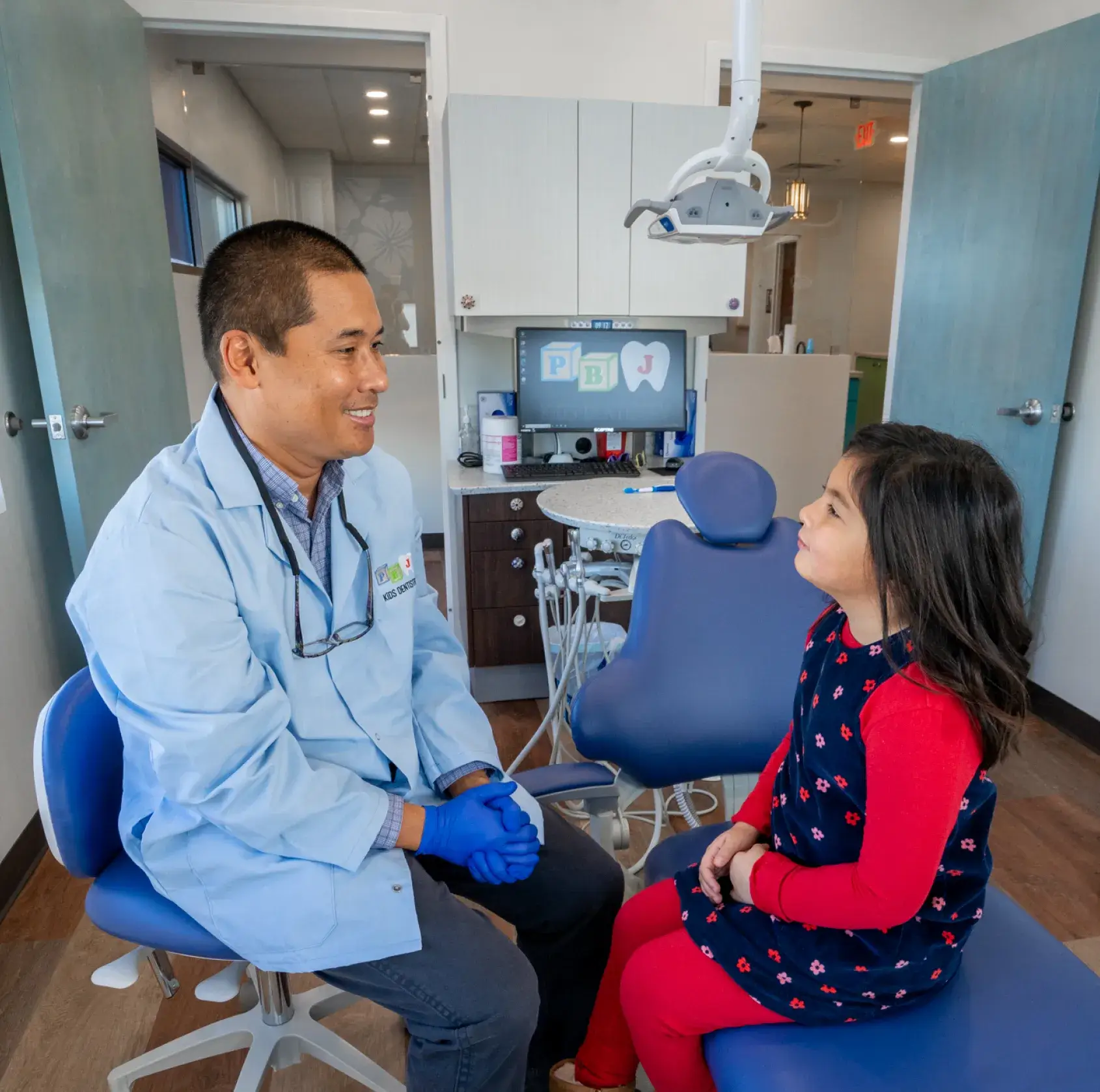 A young girl sitting on a blue chair next to a doctor.