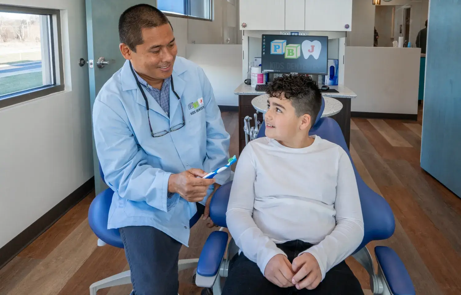 A young boy sitting in a chair with a doctor in the background.
