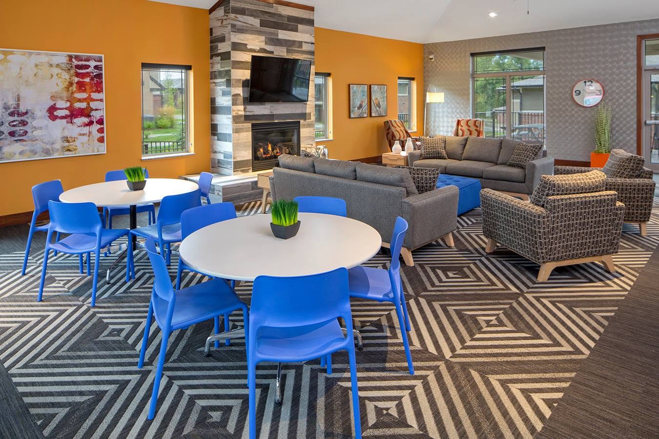Modern lounge with blue chairs around round tables, gray sofas, patterned carpet, and a fireplace.