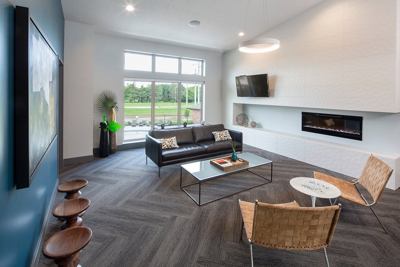 Modern living room with a black sofa, glass coffee table, two wicker chairs, and a wall-mounted TV and fireplace.