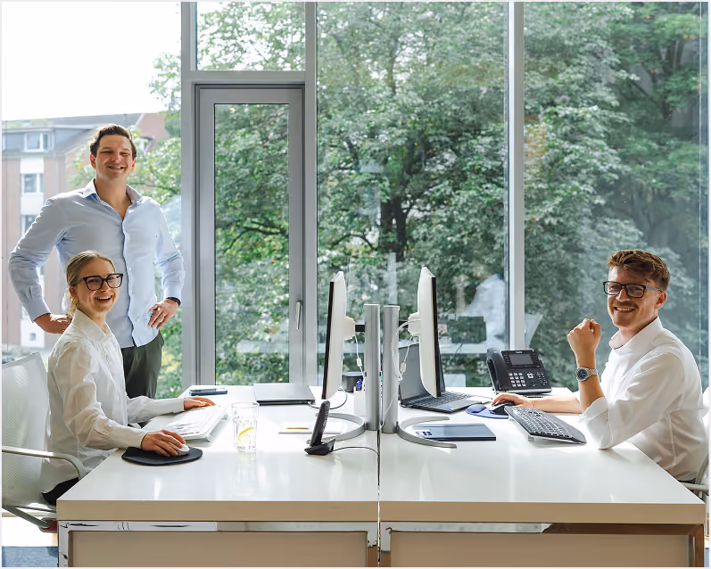 Vier Teammitglieder arbeiten an Schreibtischen in einem hellen Büro.