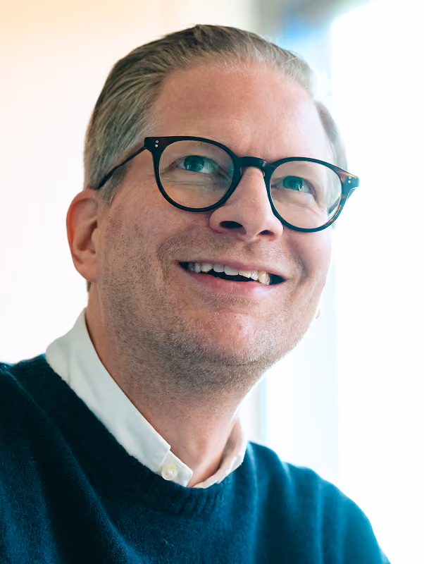 Porträt eines Mannes mit Brille in einem hellen Büro.