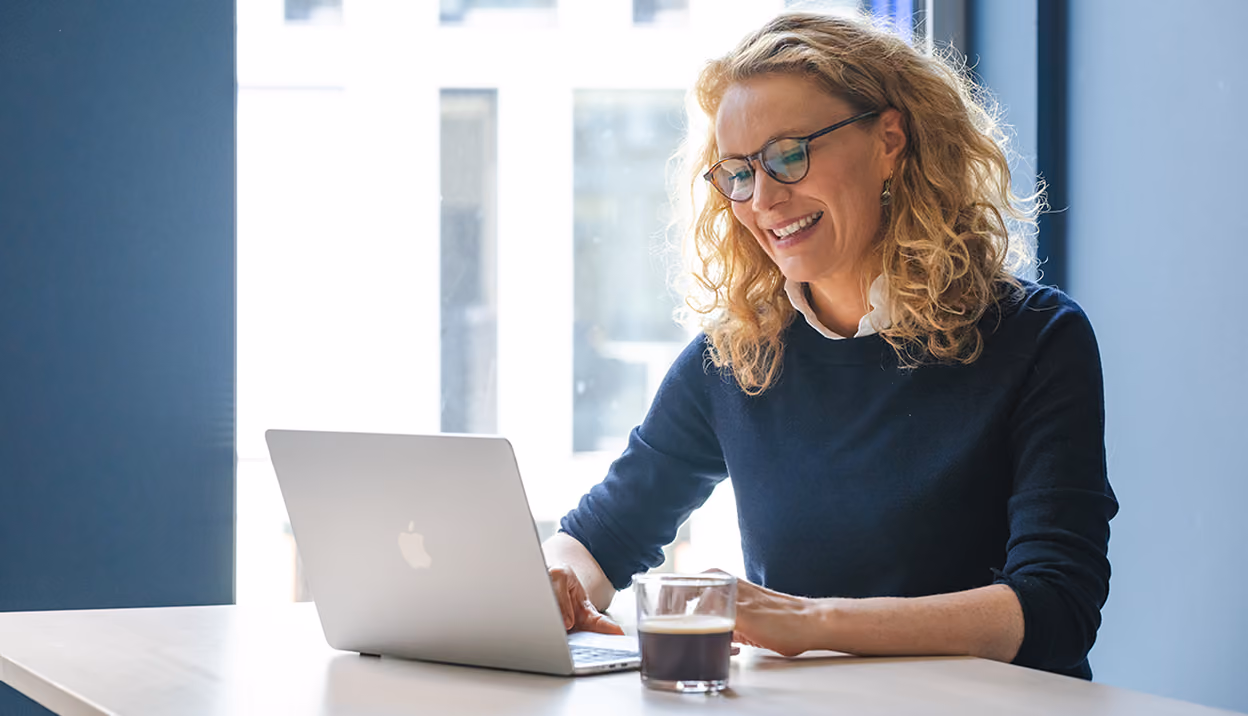 Frau mit Brille arbeitet lächelnd an einem Laptop.