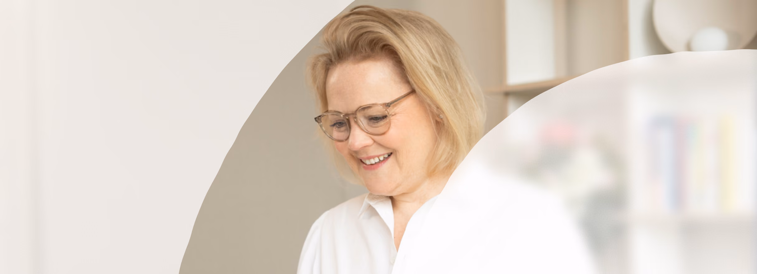Frau mit Brille sitzt an einem Laptop in einem hellen Raum.