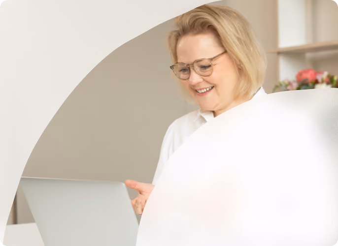 Frau mit Brille betrachtet Unterlagen an einem hellen Arbeitsplatz.