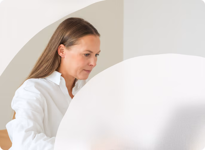 Frau sitzt am Laptop und arbeitet an einem hellen Arbeitsplatz.