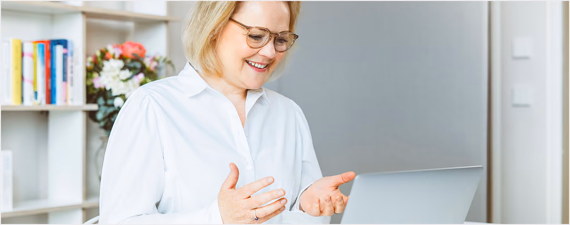 Frau sitzt lächelnd an einem hellen Arbeitsplatz.