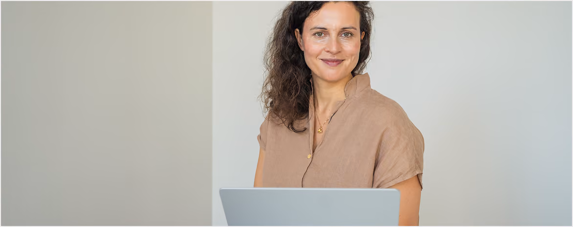Frau arbeitet an einem Laptop vor hellem, neutralem Hintergrund.