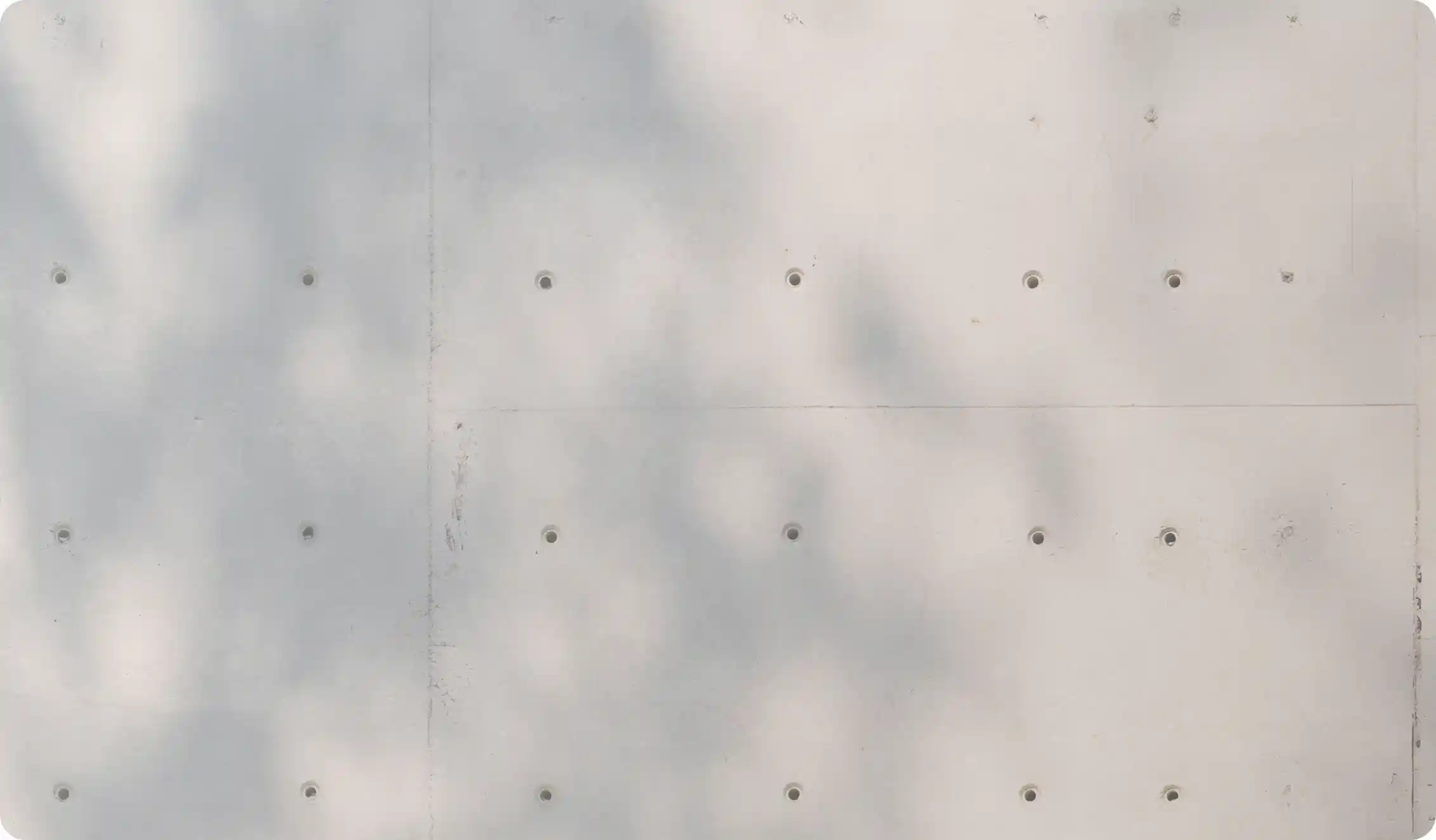 Close-up of a light gray concrete wall with regularly spaced circular indentations and subtle shadow patterns.