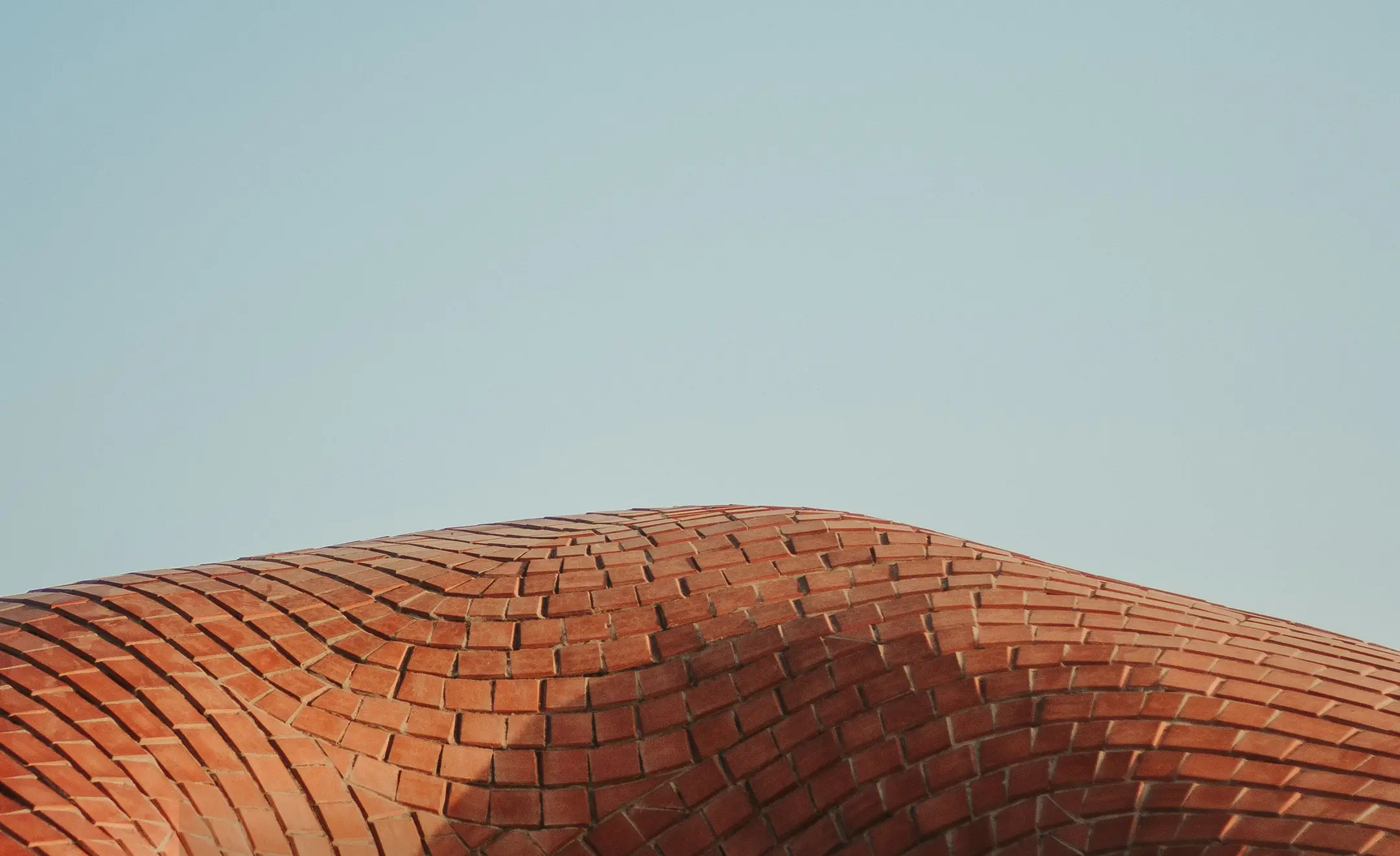 Close-up of a building roofline featuring a series of angular, folded concrete panels casting shadows.