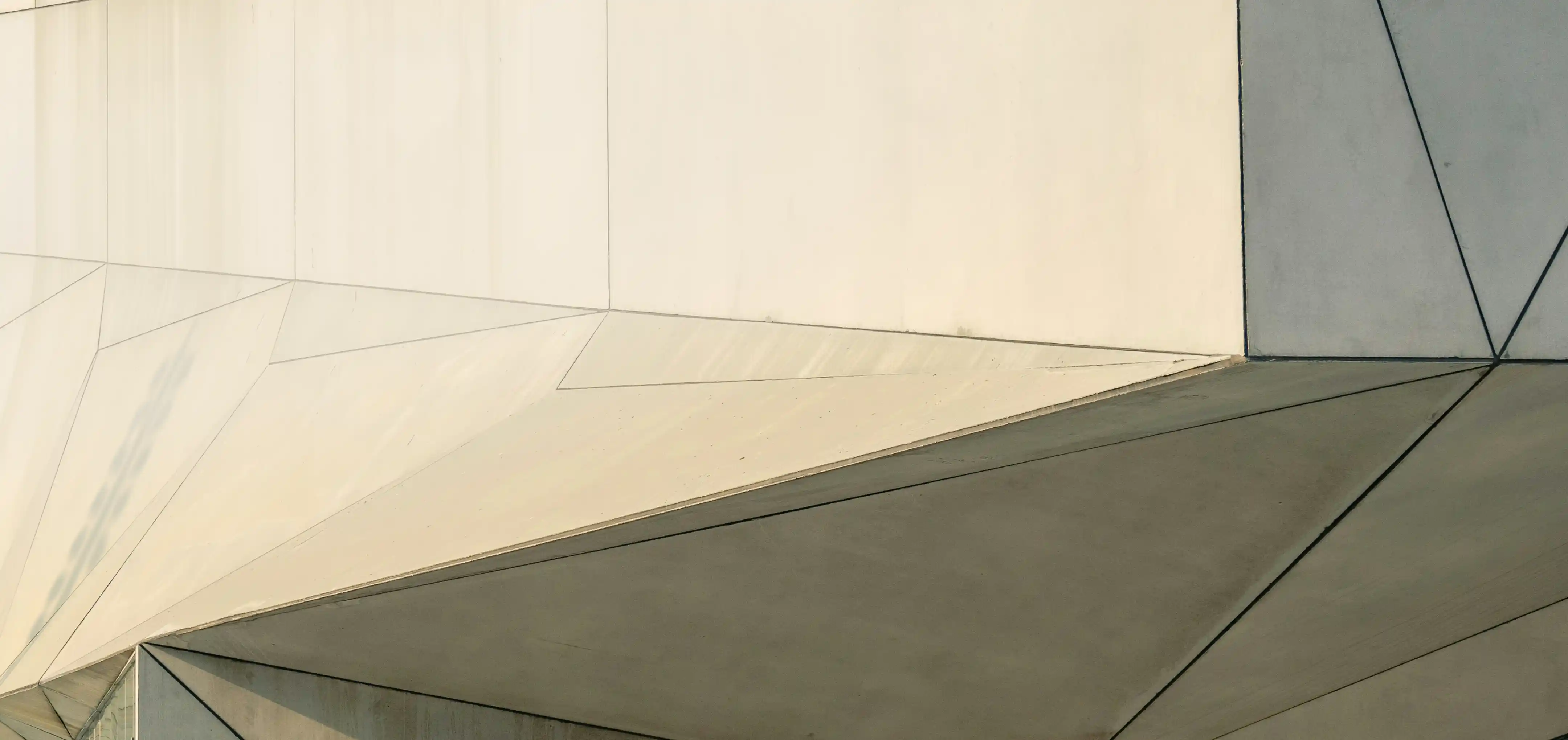 Close-up of a modern building facade showing angular, geometric concrete panels with clean lines and shadows.