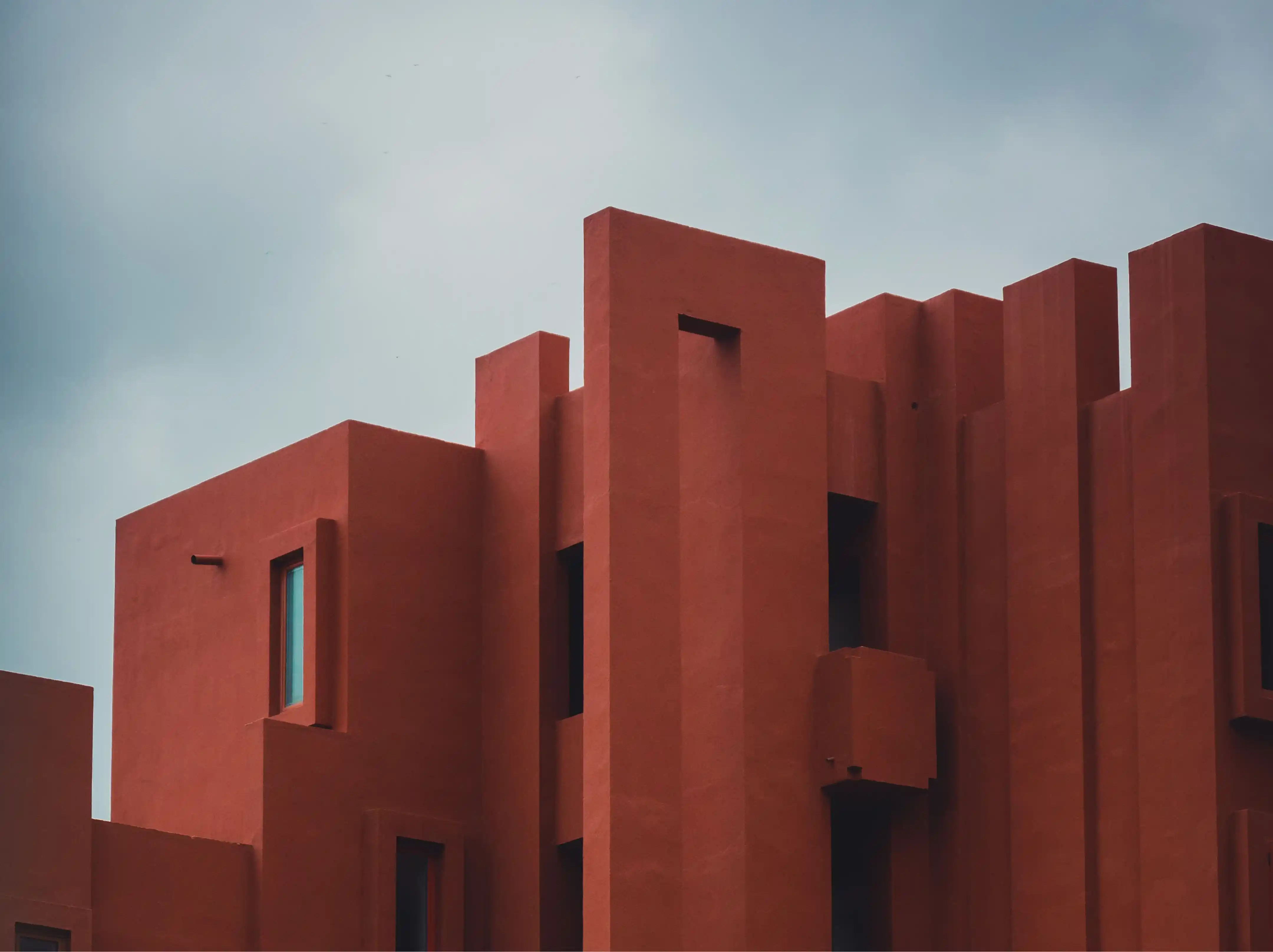 Modern building with bold architectural design featuring vertical and rectangular shapes in reddish-brown color against a cloudy sky.