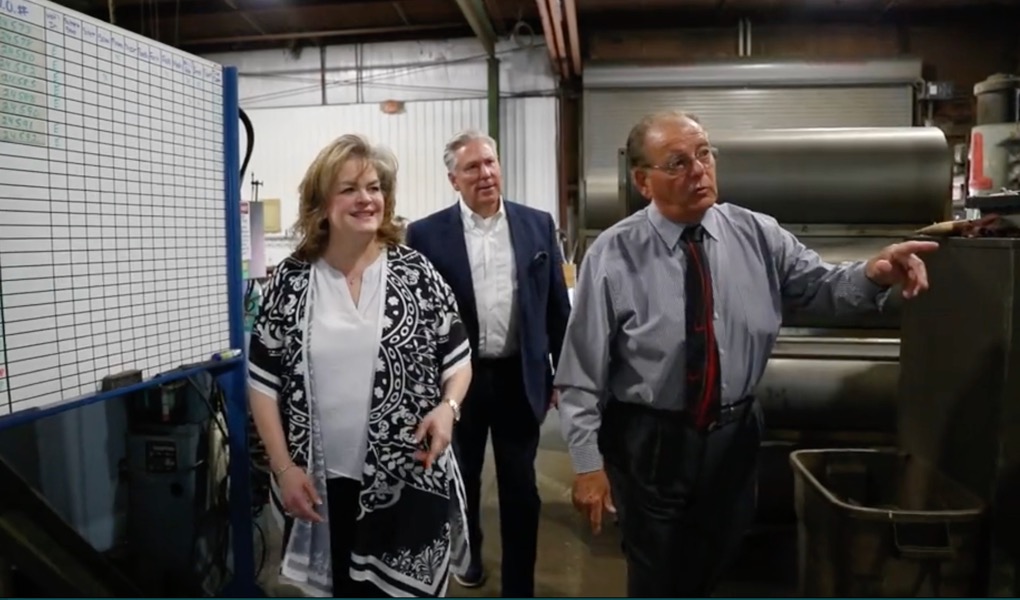 Walt Camp showing Frances Brunelle around his plant, pointing out equipment on the shop floor.