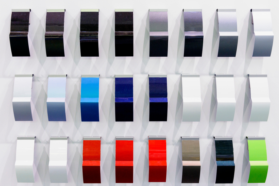 Metal finishing color samples in black, silver, blue, red, white, gray and green displayed on a wall