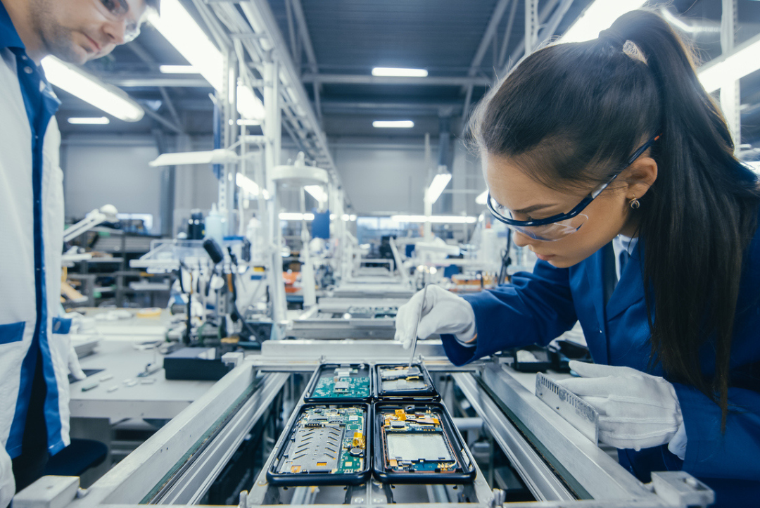 Manufacturing technician assembling electronic components on a production line while another worker observes in a modern factory