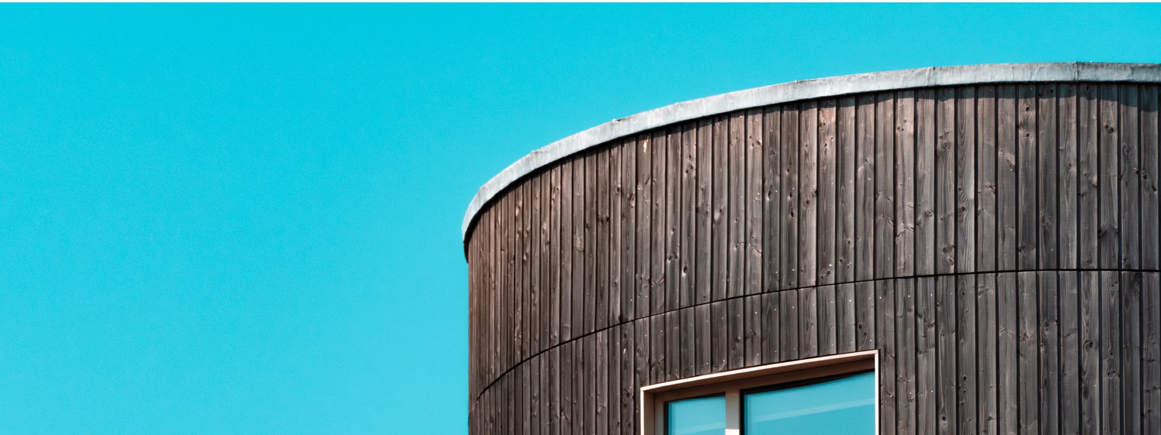 Close-up of a curved building exterior with vertical wood cladding against a clear sky