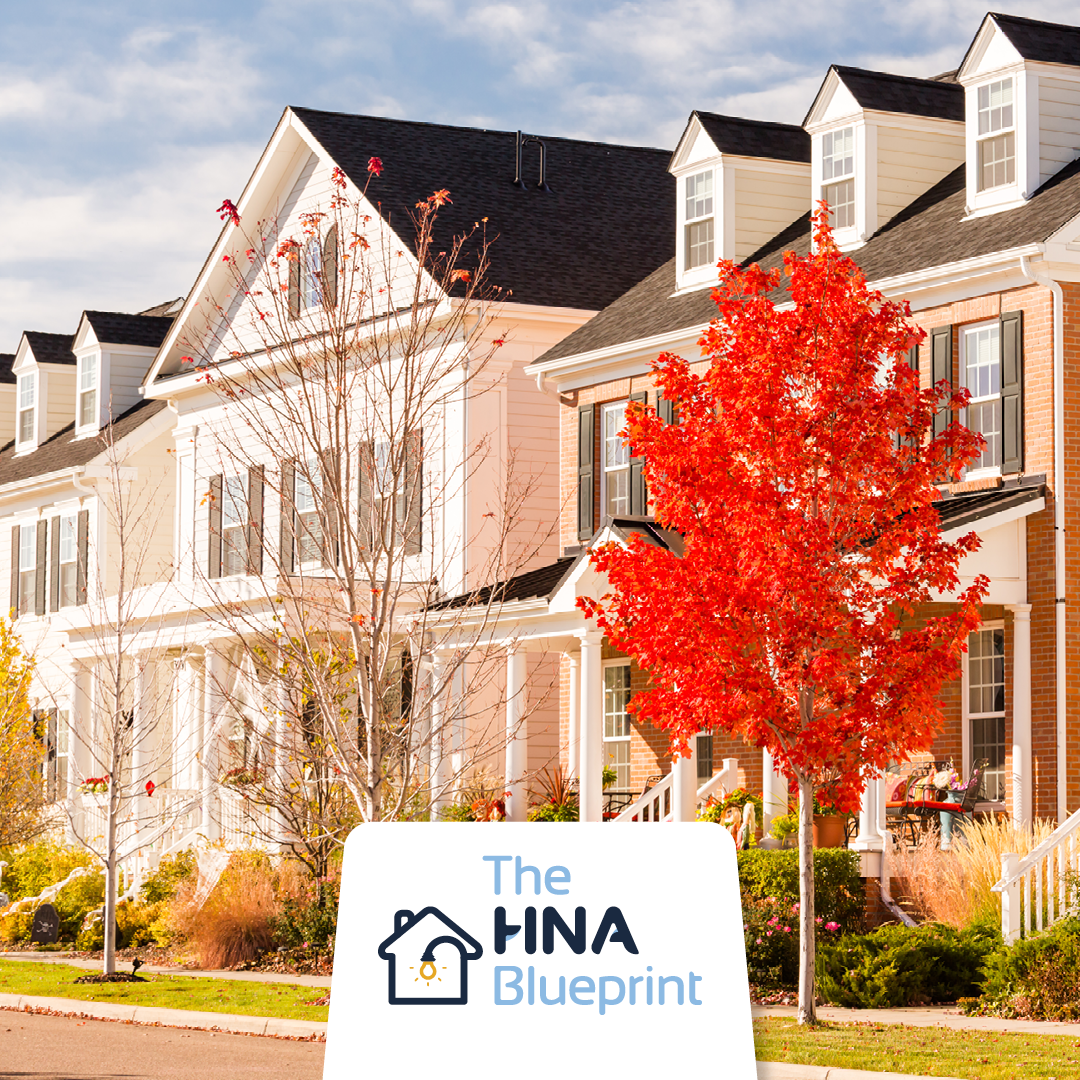 Row of suburban townhouses in autumn with The HNA Blueprint signage in the foreground