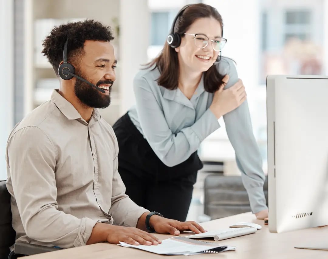 Two support team members with headsets smiling while looking at a computer screen