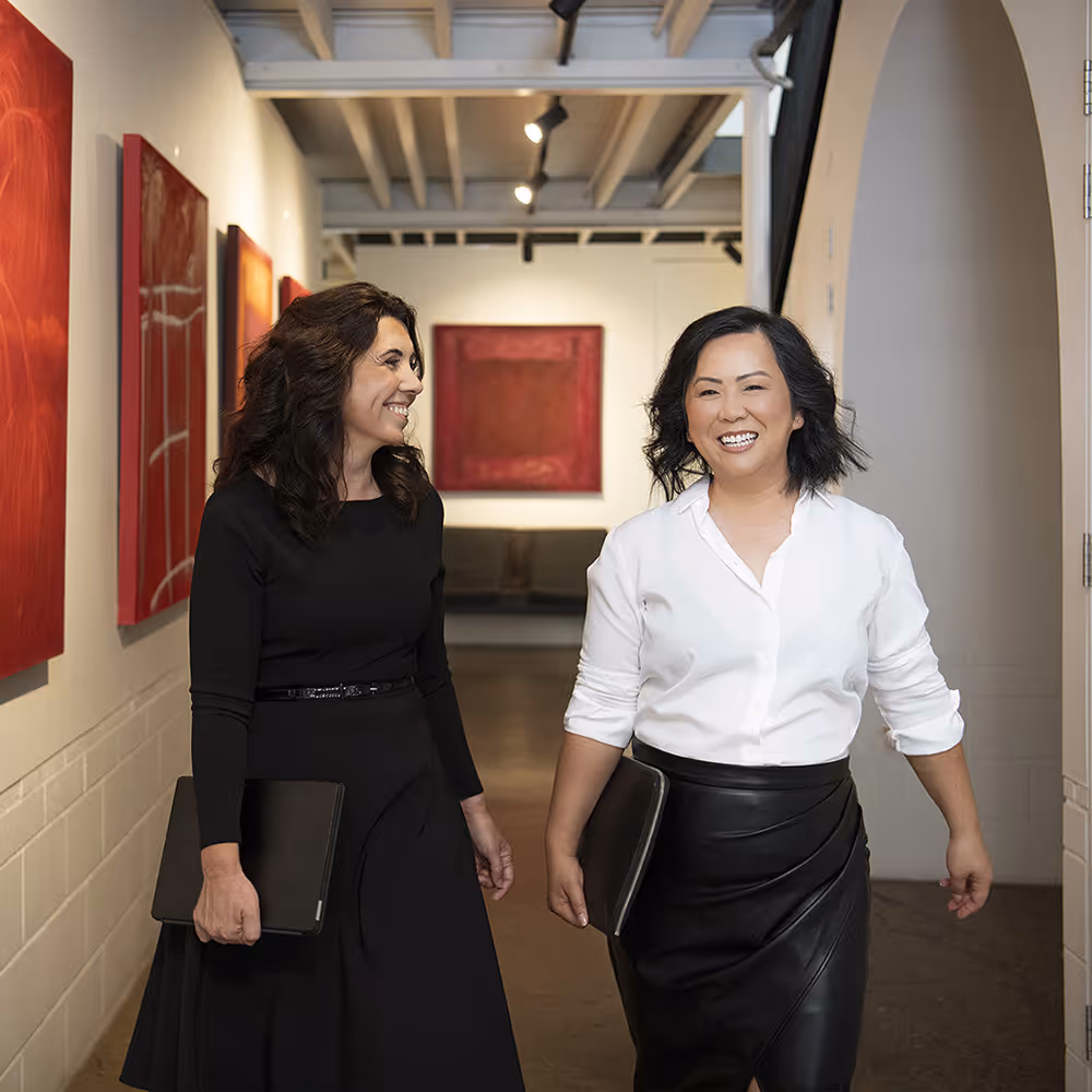 Two Catalyst Migration team members smile as they walk down a hallway holding tablets, with red artwork on the walls.