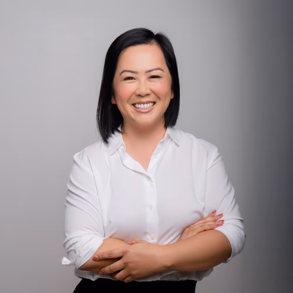 Phi Vo is smiling, wearing a white shirt, arms crossed, against a grey background.
