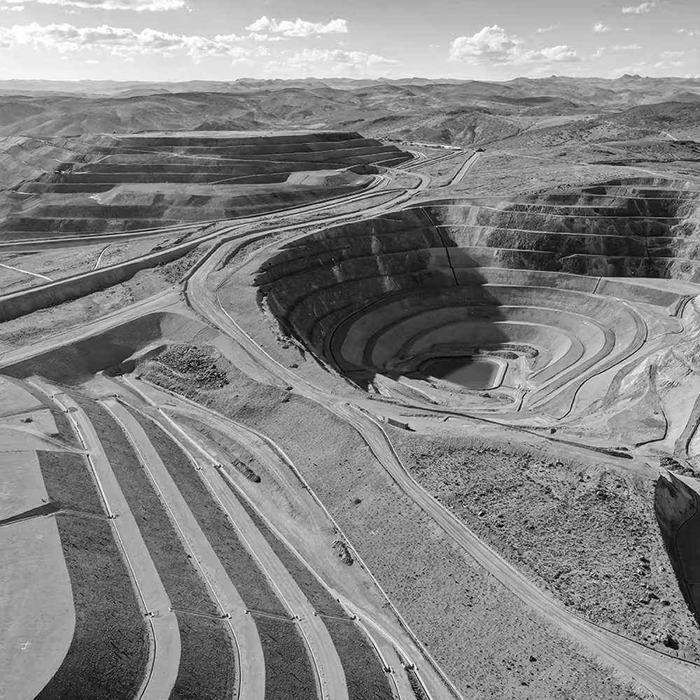 Aerial view of a large open-pit mine with terraced slopes and winding roads, surrounded by hills.