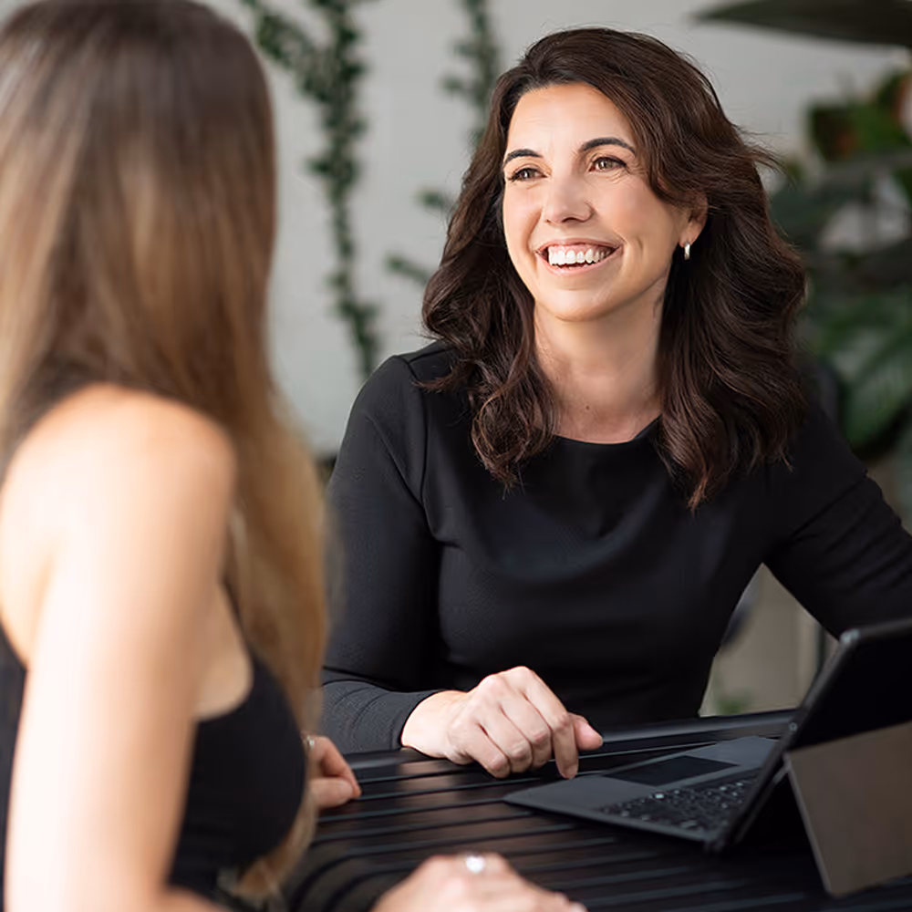 A Catalyst Migration team member in a black shirt is smiling and talking to another person at a table with a laptop.