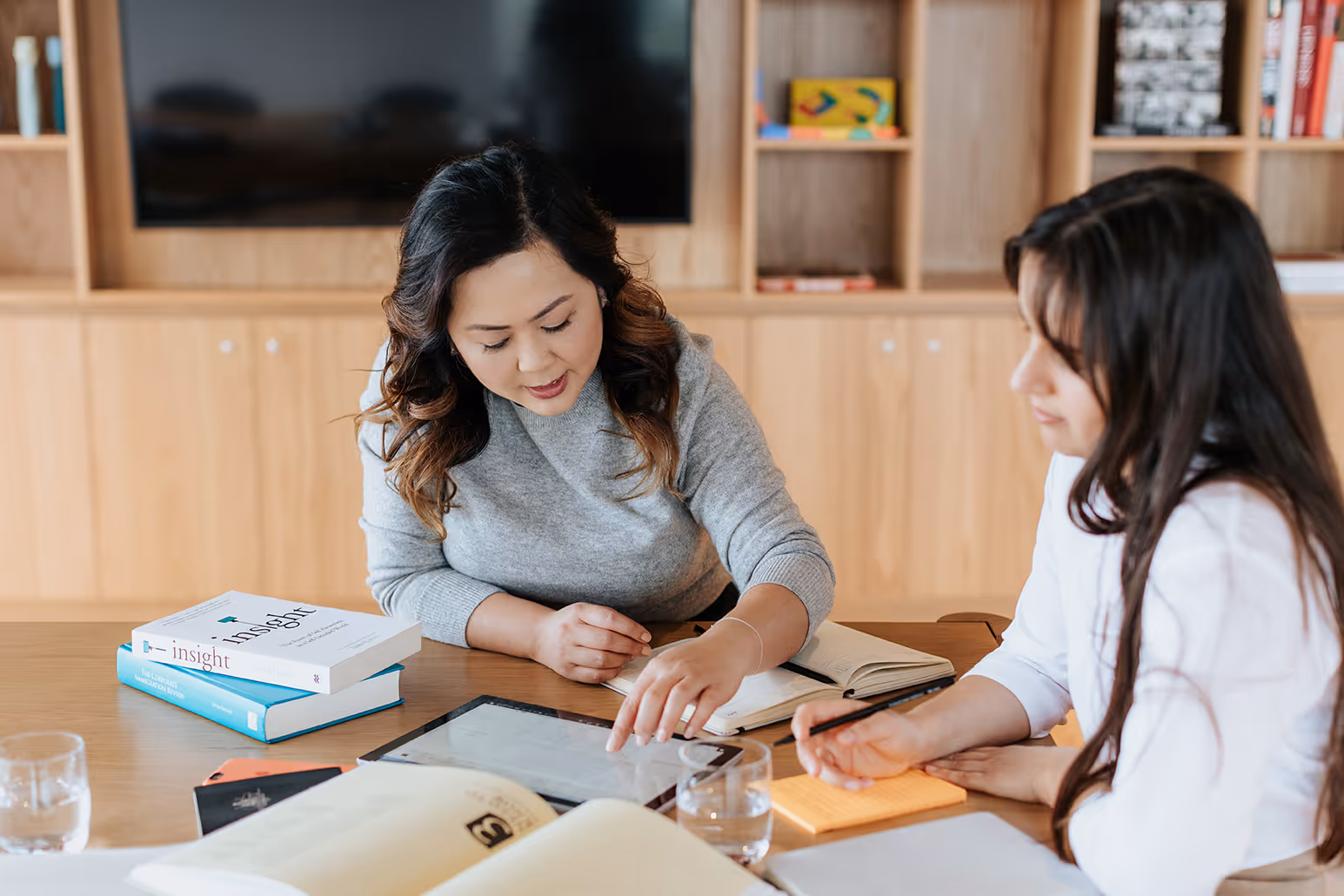 Two Catalyst Migration team members sit at a table, studying with books, notebooks, and a tablet in a room with wooden shelving.