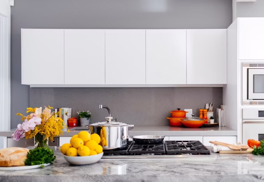 Modern kitchen with white cabinets, granite counter, gas stove, lemons, flowers, and orange cookware.