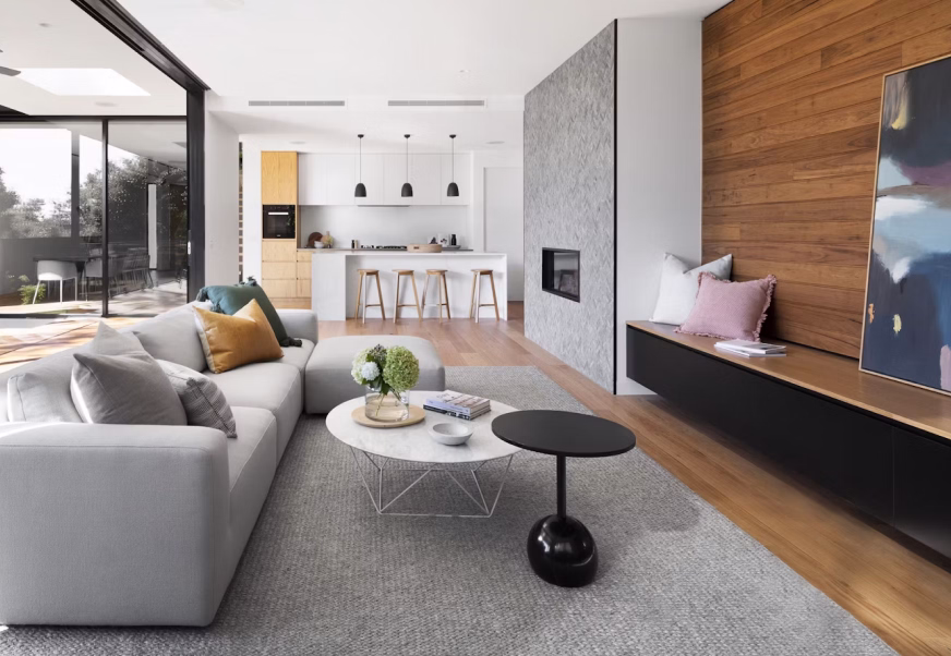 Freshly cleaned open-plan living room with a grey corner sofa and warm wood-panel wall