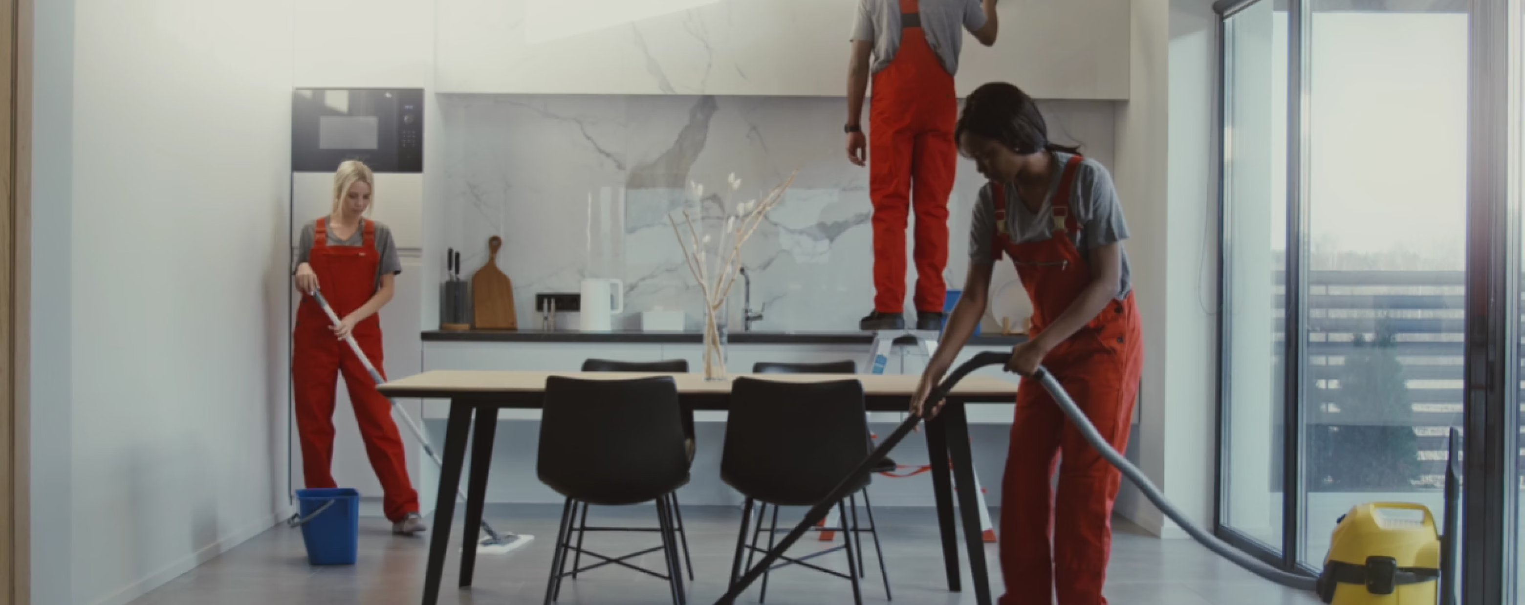 Two suited Dustora cleaners vacuuming and wiping down a bright dining area