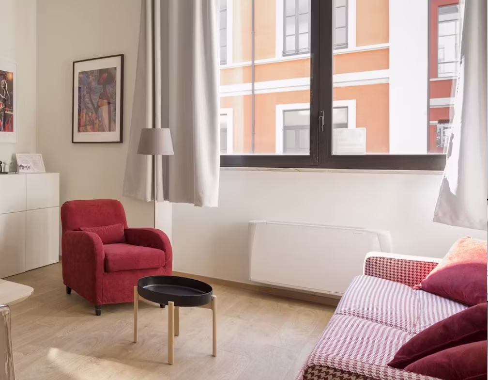 Tidy living room with a red armchair, dusted shelves and a made-up sofa