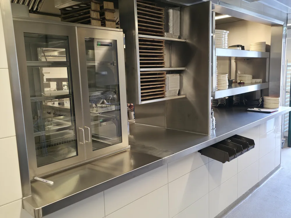 Wärmeschrank mit Glastüren neben einem Edelstahlregal in der Großküche