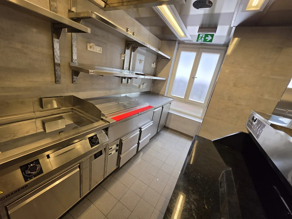 Kochzeile mit Grillplatte unter der Lüftungshaube in einer Großküche