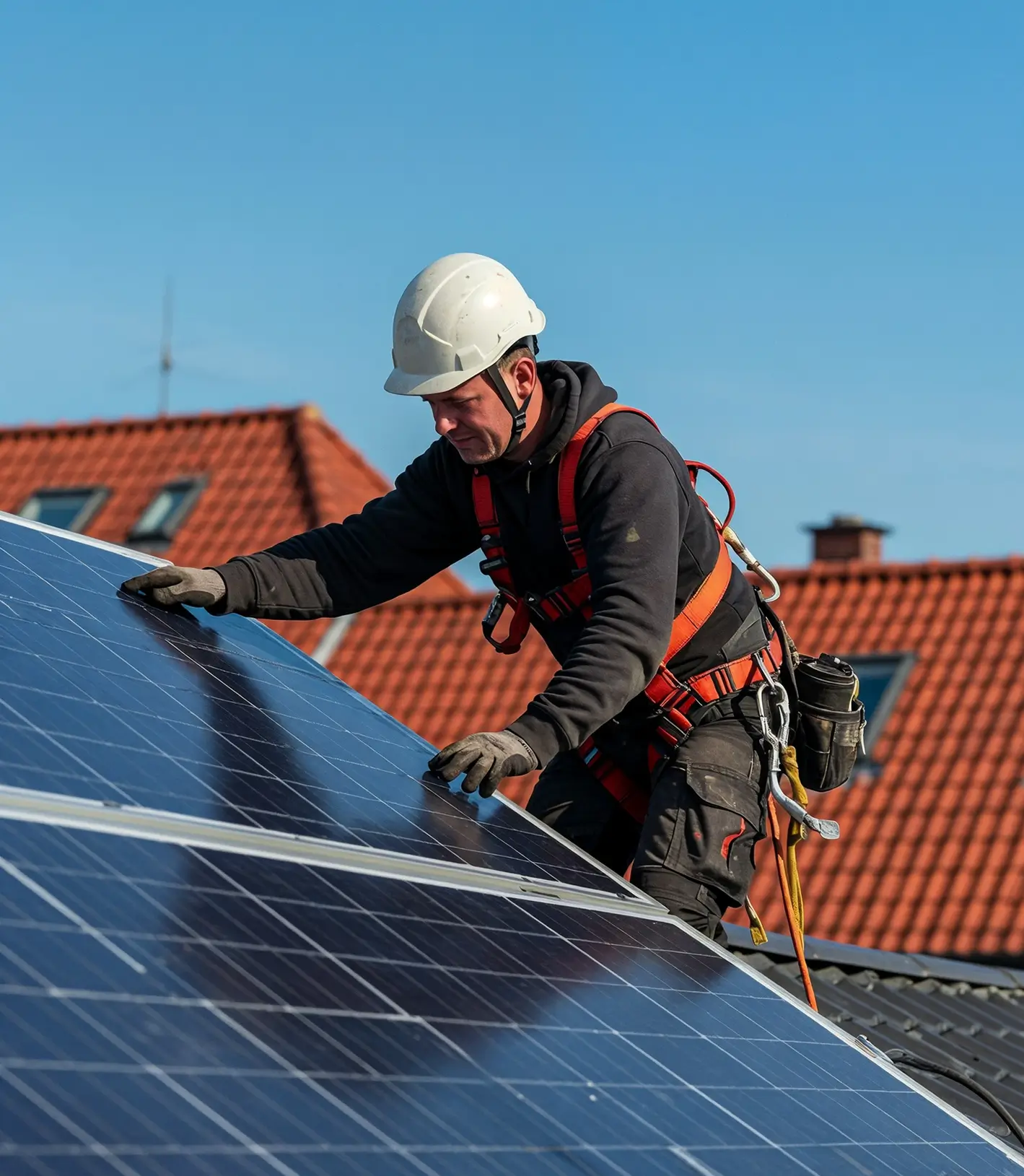 Worker in safety gear installing or inspecting solar panels on a rooftop under clear blue sky.