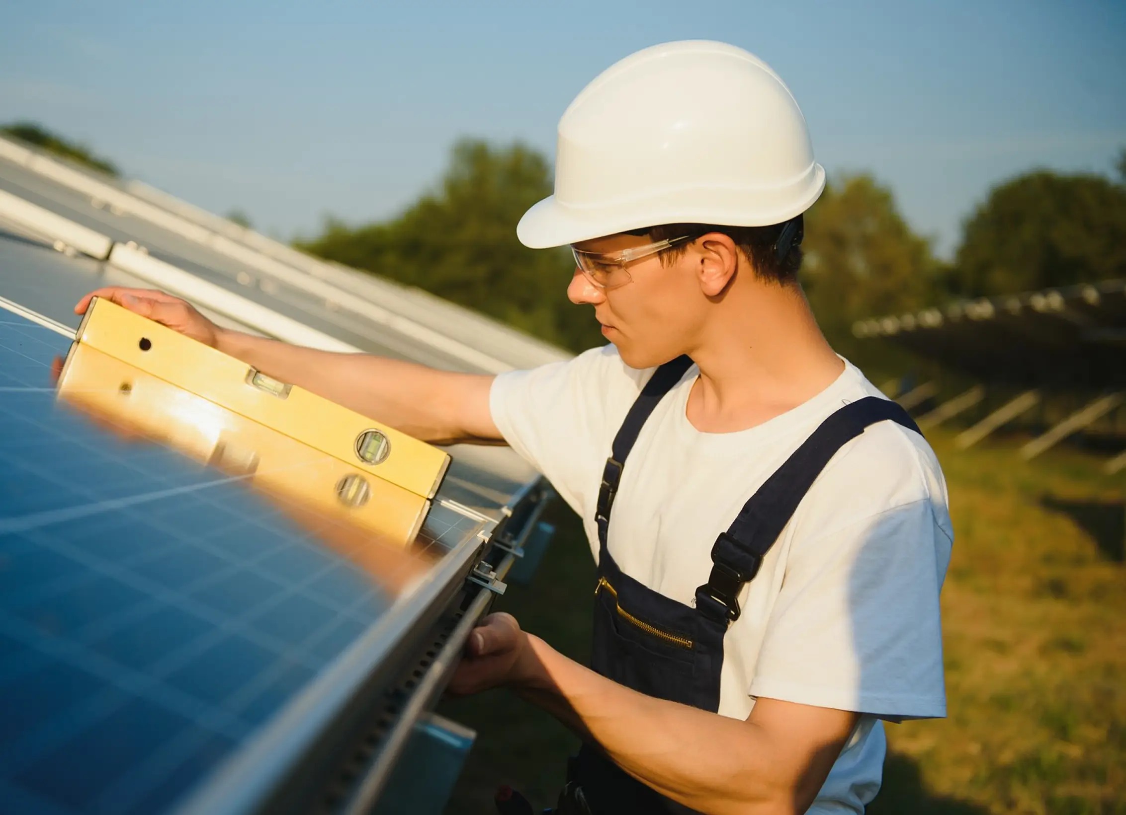Technician wearing hard hat checks solar panel alignment with a level tool outdoors.