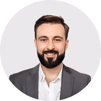 Smiling man with dark hair and beard wearing a white shirt and gray suit jacket.