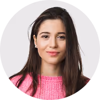 Portrait of a young woman with long brown hair wearing a pink sweater, smiling slightly.