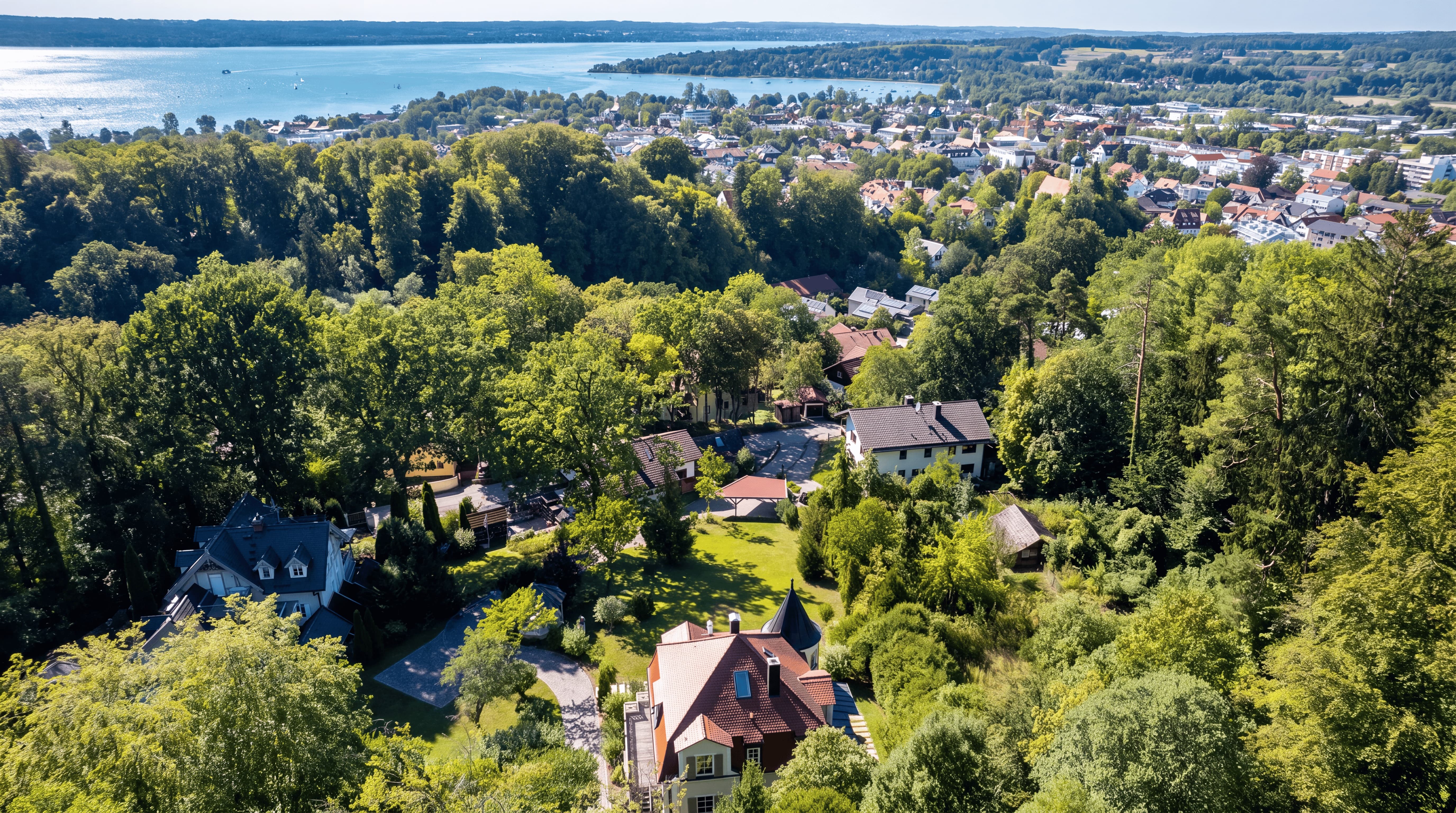 Luftaufnahme einer grünen Wohngegend mit Bäumen und einem See im Hintergrund an einem sonnigen Tag.