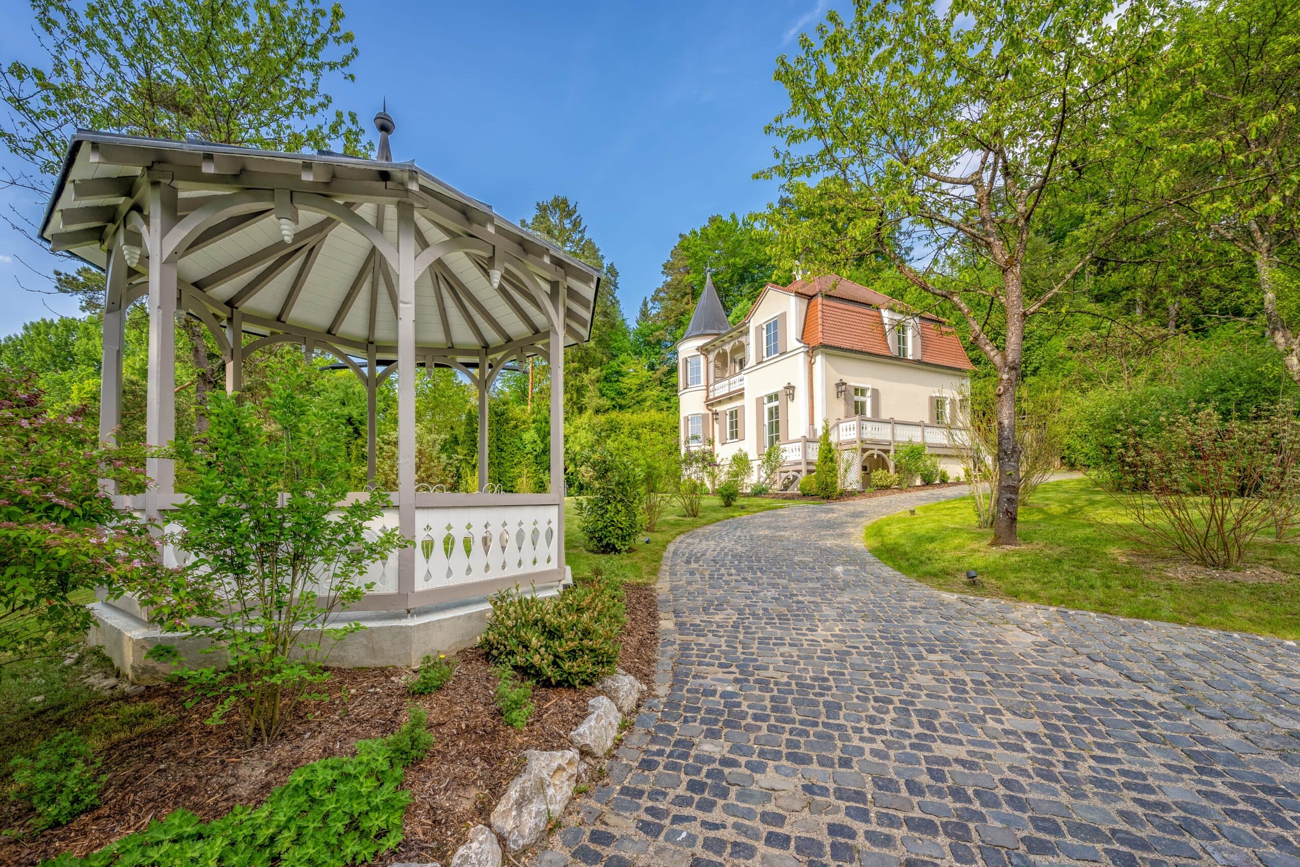 Weißes Haus im Landhausstil mit Turm und gepflastertem Weg durch grünen Garten.