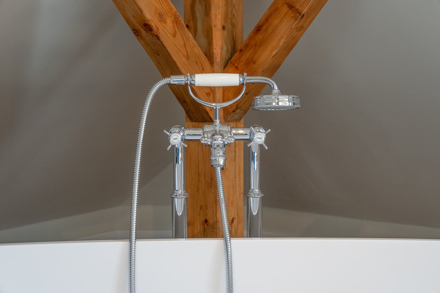 Verchromter Wasserhahn mit Handbrause über weißer Badewanne vor hölzernem Träger.