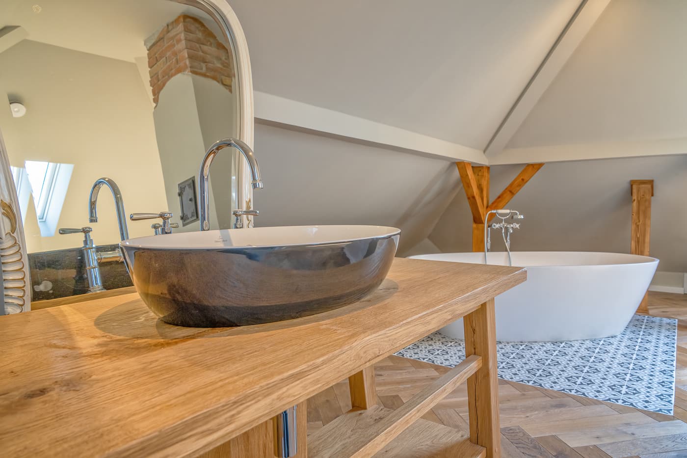 Modern Badezimmer mit ovalem Waschbecken auf Holzplatte und freistehender Badewanne auf gemustertem Boden.
