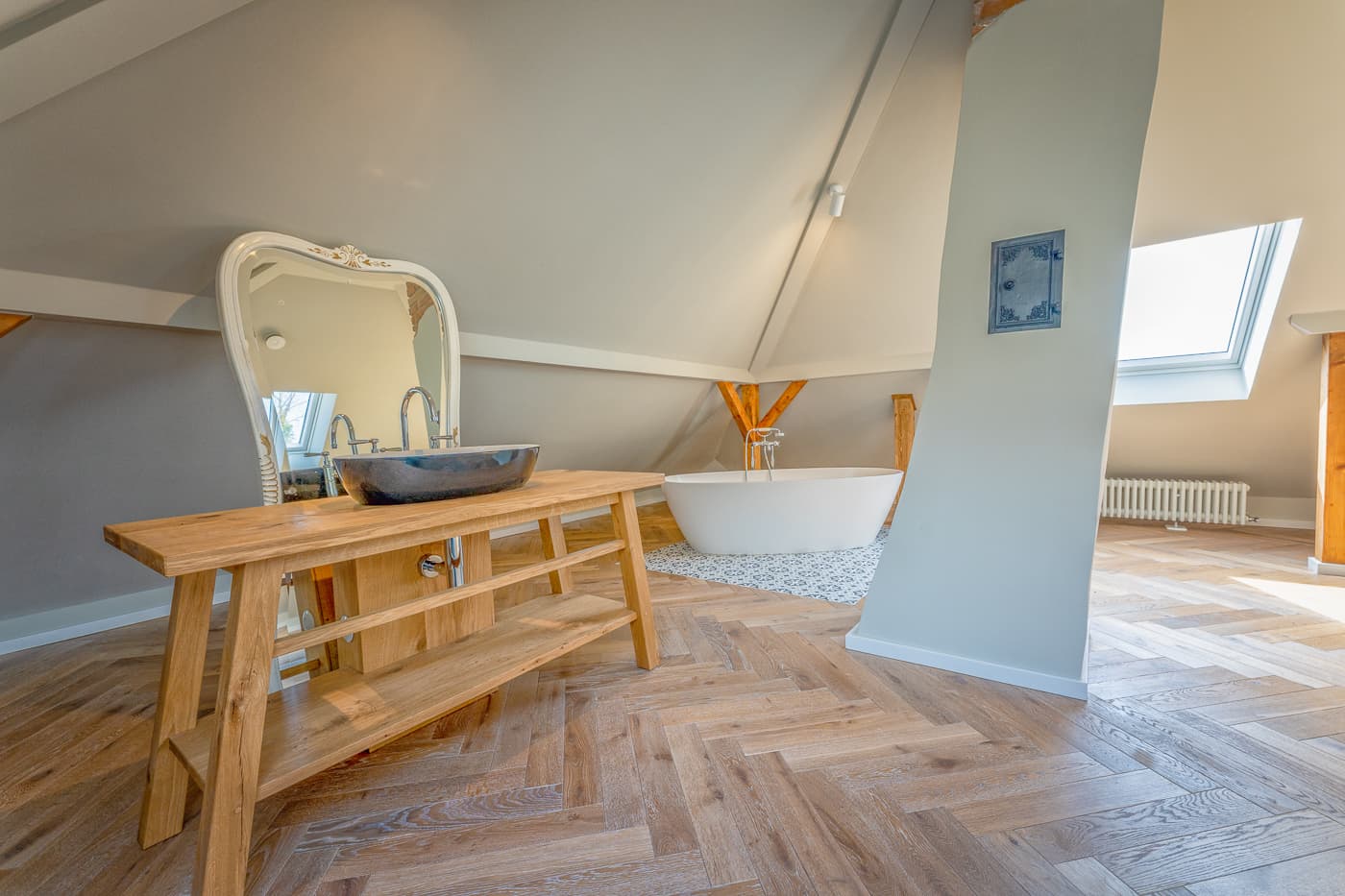 Modern bathroom with wooden vanity, black sink, large mirror, freestanding white bathtub, skylight window.