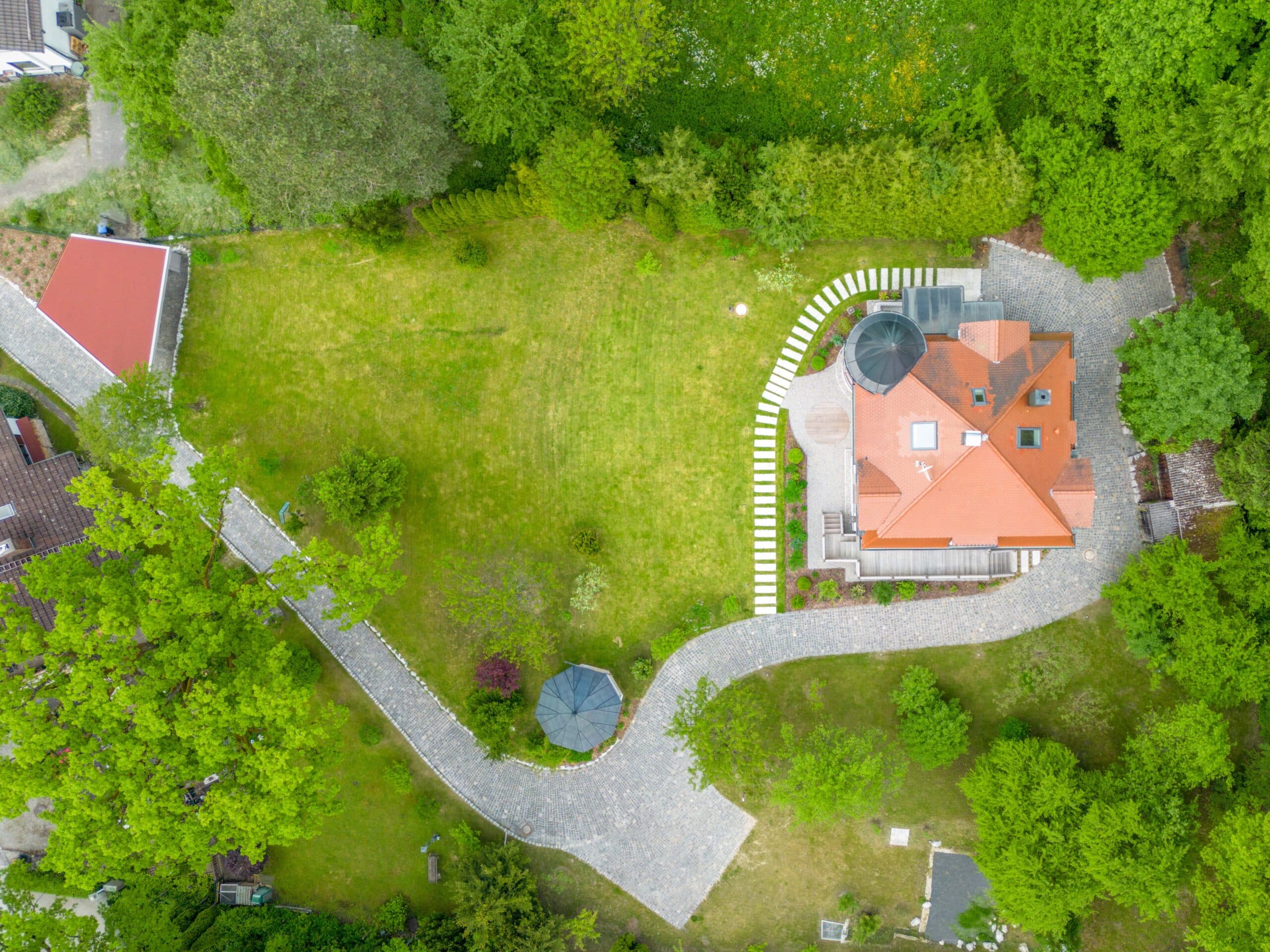 Luftaufnahme eines Hauses mit rotem Dach, gepflastertem Weg und umliegendem Grün.